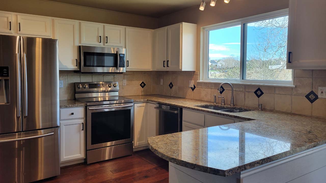 Wide view pf a kitchen with newly painted cabiets. Light reflects off the surface of the marble counter.