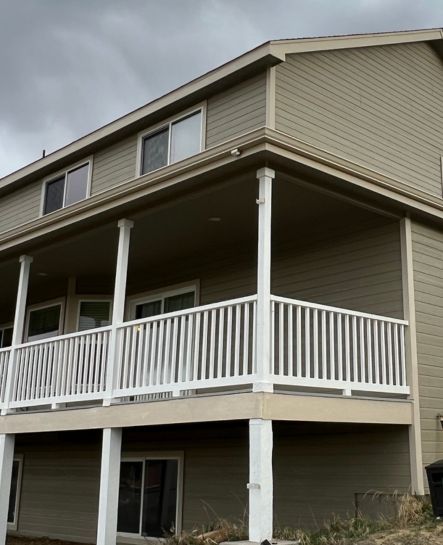 A two-story house with wraparound deck porch under cloudy sky.