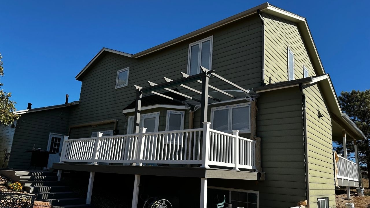 A street view under a vibrant blue sky features a beautifully painted deck by Elk Horn Painting. The fresh green exterior shines with a fresh, professional finish.