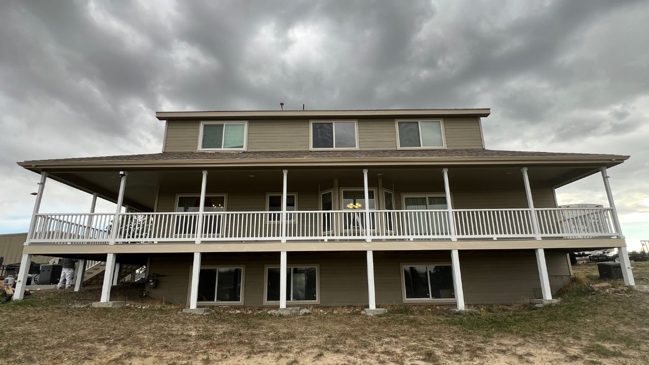 A two-story house with wraparound deck porch under cloudy sky.