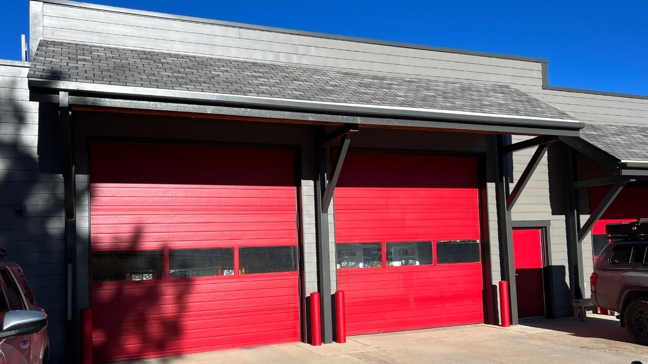 Exterior view of a commercial building newly painted in red and gray. The sky is blue with clouds positioned directly above the garage.