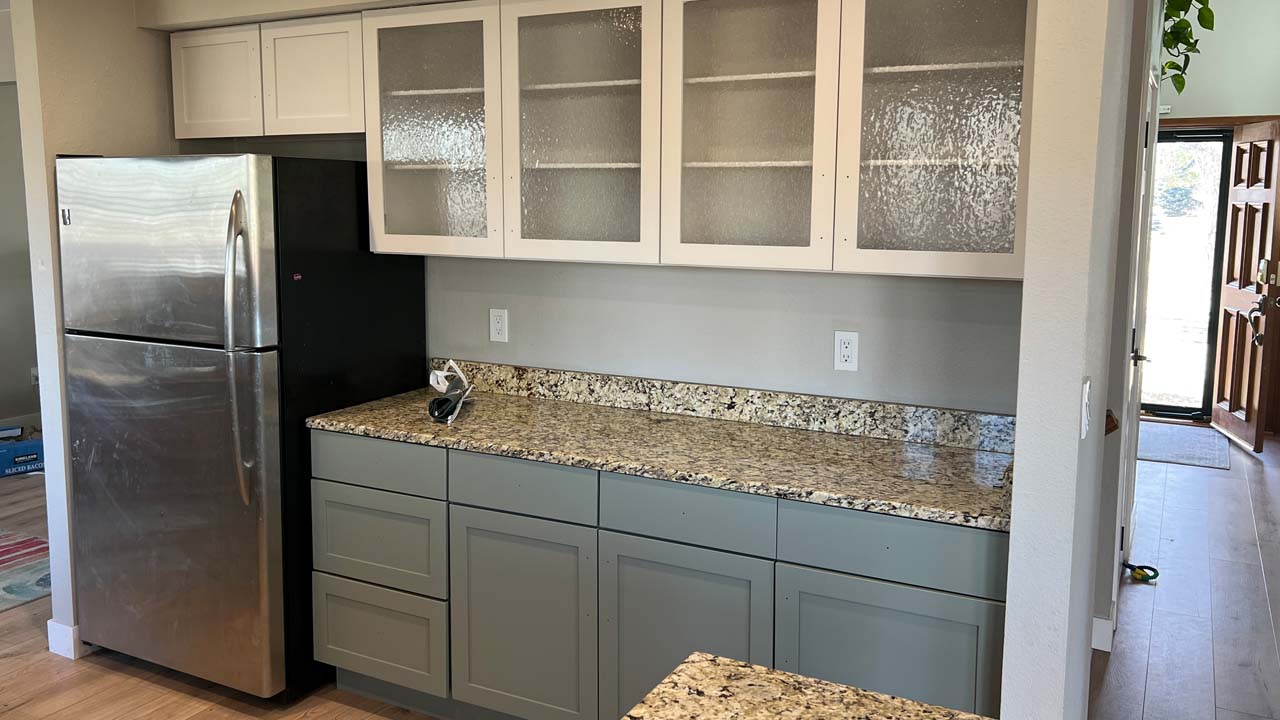 Image of a kitchen area and cabinets that have been repainted. On the right we can see down teh entrywau to an open door.