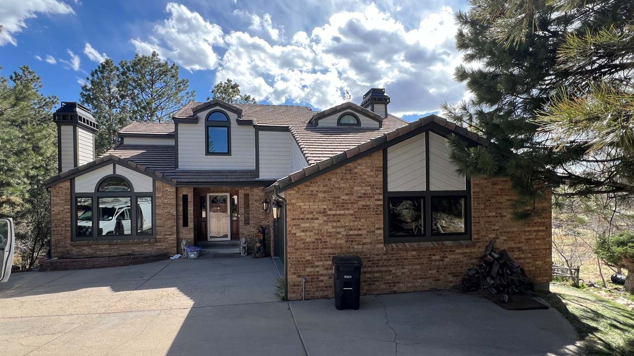 Exterior view of a home that has been repainted. The sky is blue with clouds and the home is nestled in tal pine trees.