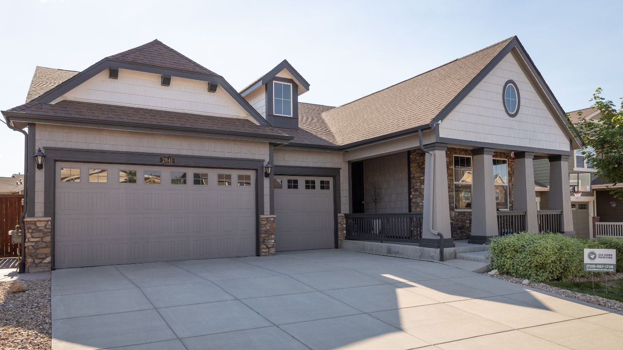 A street view under a vibrant blue sky features a beautifully painted home by Elk Horn Painting. The beige exterior shines with a fresh, professional finish.